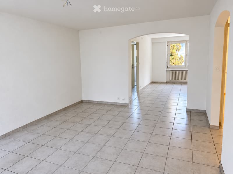 Empty hallway with tiled flooring and white walls, featuring an arched doorway leading to another room with a window and radiator.
