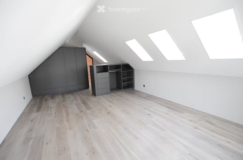 Bright attic room with wooden flooring, white walls, built-in wardrobes, and skylight windows.