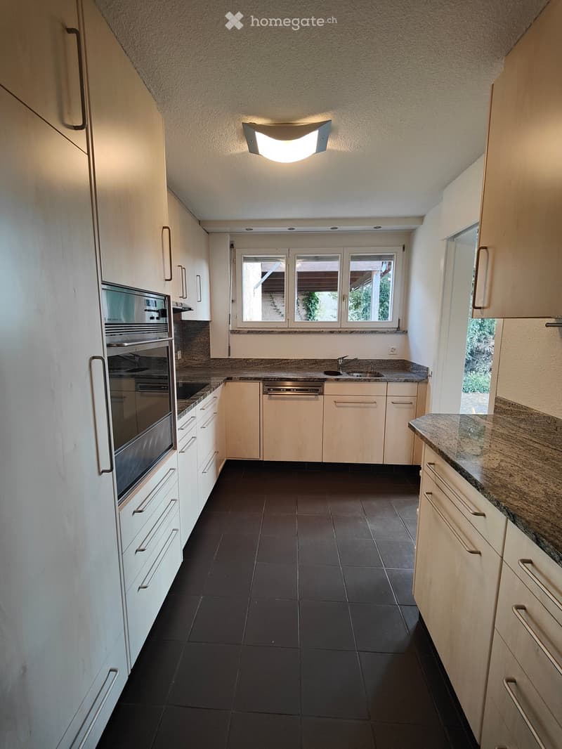 Modern kitchen with white cabinets, dark tiled floor, granite countertop, built-in oven, dishwasher, and sink.