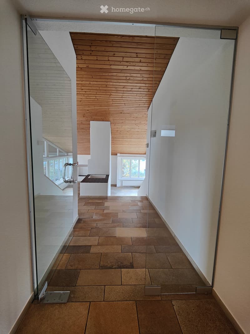 Modern hallway with tiled floor, glass sliding doors, and wooden ceiling. Features a small bench and window with view.