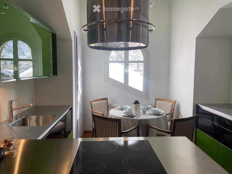 Modern kitchen with green cabinets, stainless steel appliances, induction stove, sink, and a small dining area with a table and chairs.