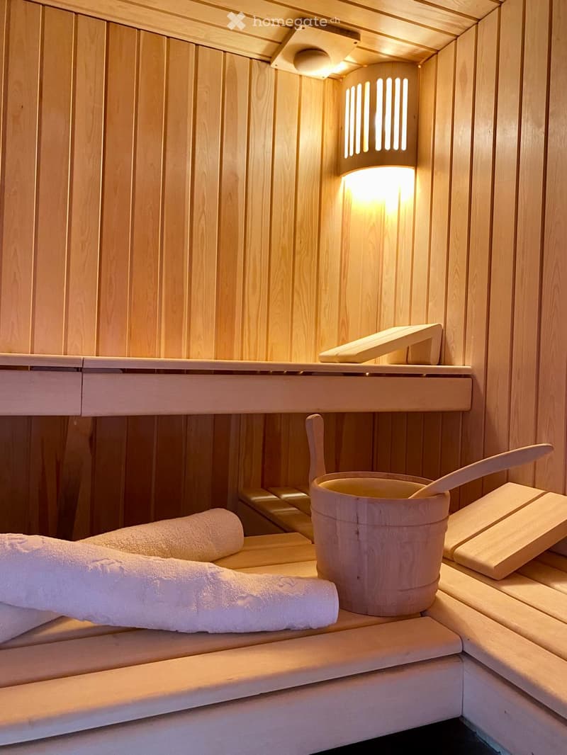 Wooden sauna interior with a wooden bucket, paddle, and towels on the bench.