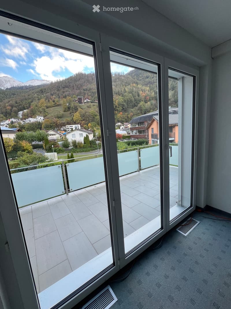 Empty room with large glass doors leading to a tiled balcony, offering a scenic mountain view.