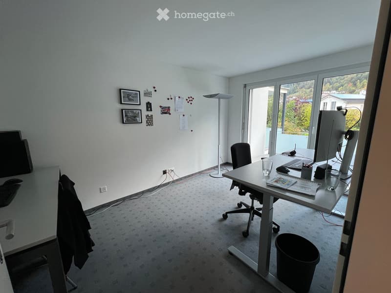 Modern office space with a desk, chair, computer, and large windows offering a scenic view.