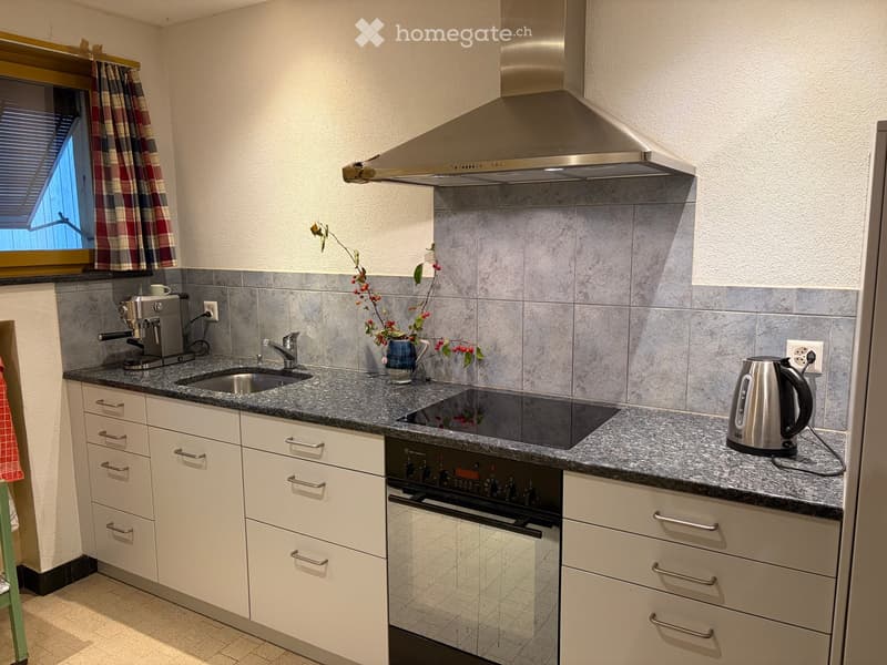 Modern kitchen with white cabinets, granite countertop, stainless steel appliances, and a window with plaid curtains.