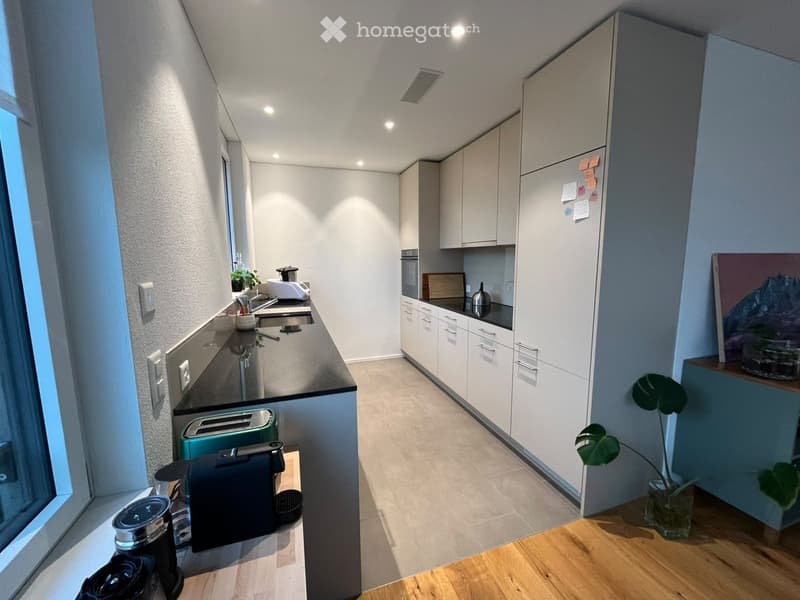 Modern kitchen with white cabinets, dark countertops, and various appliances including a coffee machine, toaster, and sink.