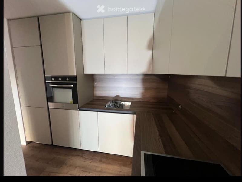 Modern kitchen with white cabinets, a built-in oven, and a stove, featuring wooden flooring and sleek design.
