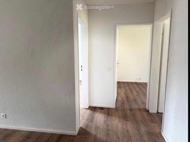 Empty hallway with wooden flooring, white walls, and multiple open doors leading to other rooms.