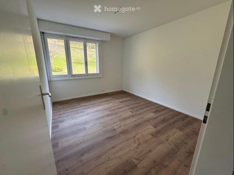 Empty room with wooden flooring, white walls, and a large window letting in natural light. No furniture or equipment is present.
