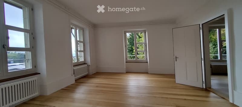 Empty room with light wooden flooring, white walls, multiple windows, and radiators. No furniture or equipment present.