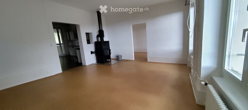 Empty room with light-colored walls, wooden flooring, and a visible fireplace in the corner. The room is unfurnished with no visible furniture or equipment.
