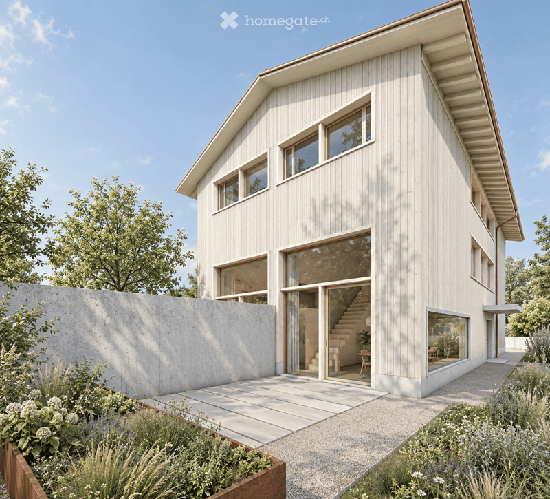 Modern two-story house with light wood siding, large windows, and a raised ground floor. Features a concrete retaining wall, garden area, and a small patio with visible interior elements like a staircase and chairs.