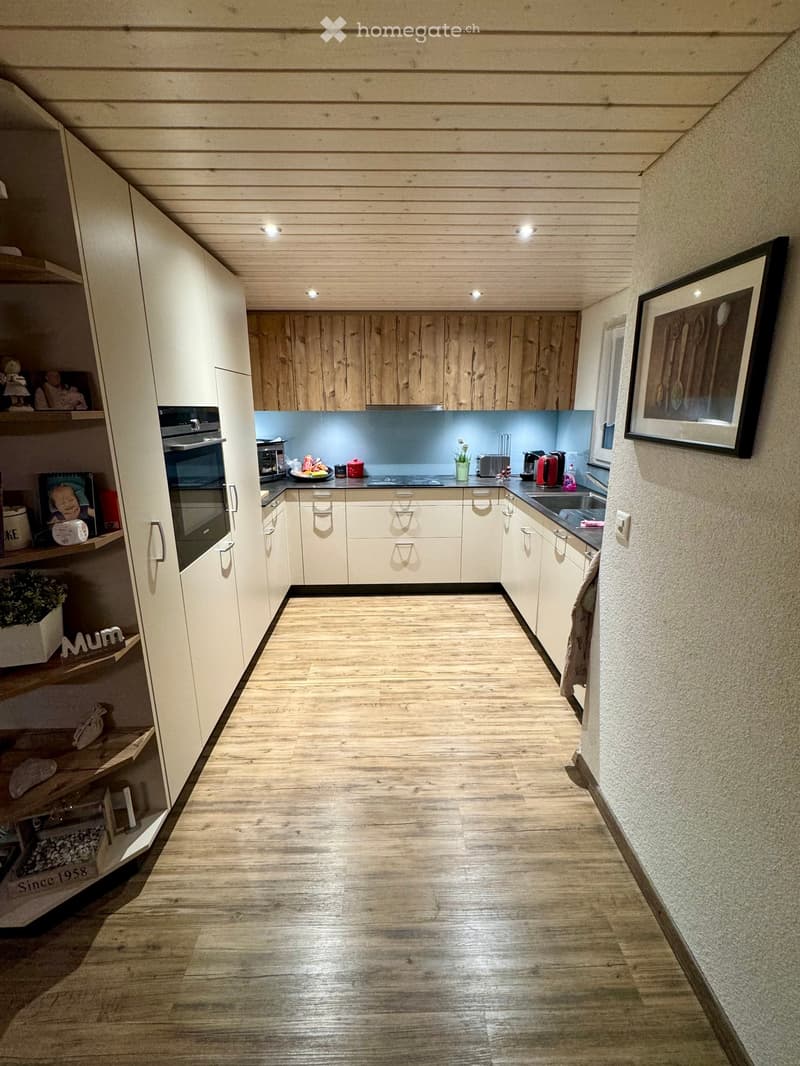 Modern kitchen with light wood cabinets, stainless steel appliances, and a wooden floor.
