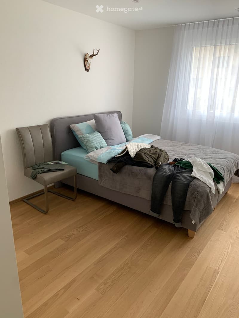 Bedroom with wooden flooring, a grey upholstered bed, a matching stool, and a deer head mounted on the wall.