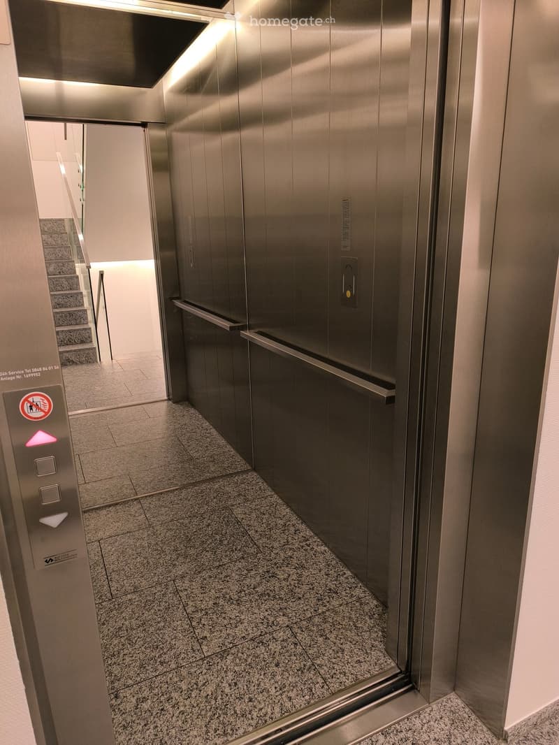 Modern hallway with polished granite tiled floor, stainless steel elevator doors, and a visible staircase in the background.