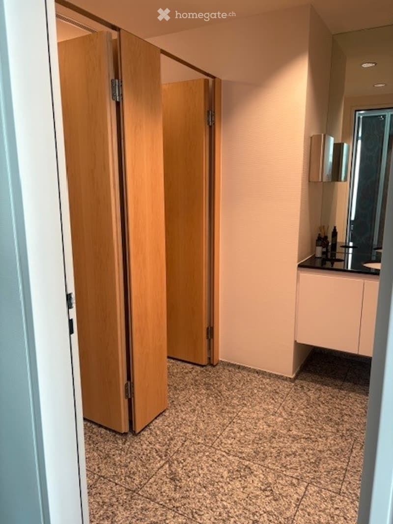 Modern bathroom with light-colored tiles, a wooden sliding door, a white sink, and a mirror above it.