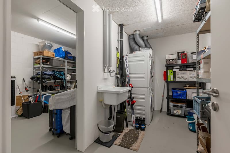 Utility room with washing machine, sink, shelves, ski, boots, and various storage items.
