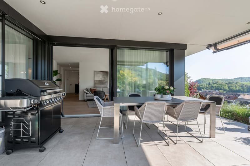 Modern outdoor terrace with a dining table, chairs, grill, and a view of the landscape.