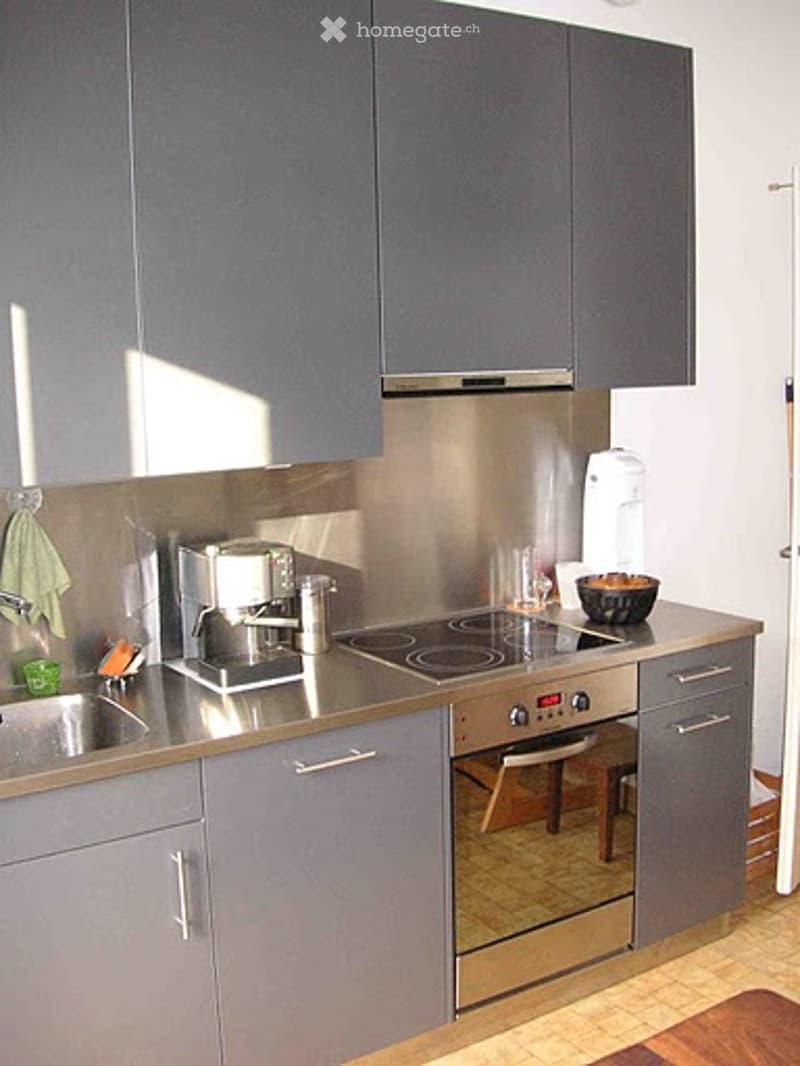 Modern kitchen with grey cabinets, stainless steel appliances, induction stove, coffee maker, and various kitchen items on the counter.