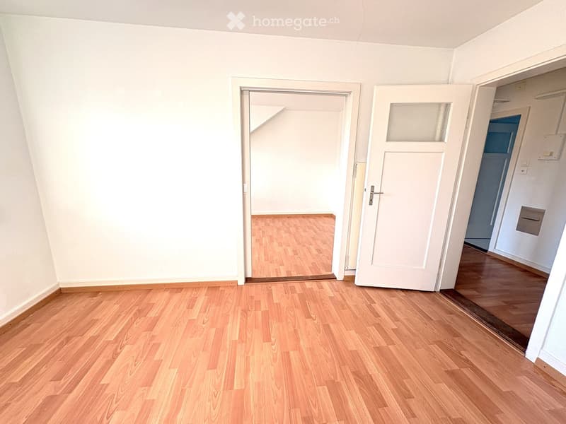 Empty room with wooden flooring and white walls, featuring two open doors leading to adjacent spaces.
