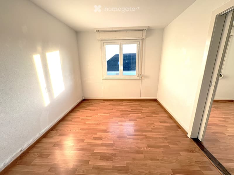 Empty room with wooden flooring, white walls, and two windows allowing natural light to enter.