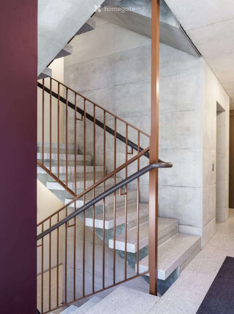 Modern staircase with concrete steps and a sleek metal railing, featuring a contemporary design with clean lines and a warm copper accent.