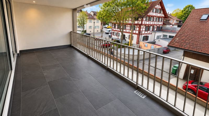 Balcony with dark tiled floor, metal railing, overlooking a street with houses, trees, and parked cars.