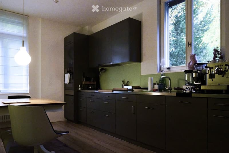 Modern kitchen with dark grey cabinets, a central island, a coffee maker, a blender, and a hanging light fixture.