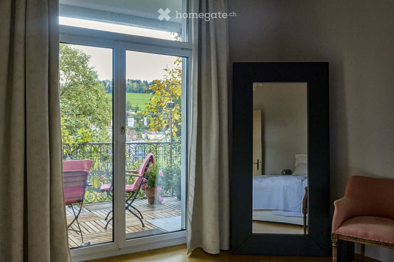 A well-lit room with a large mirror, a pink armchair, and a view of a scenic outdoor area through a sliding glass door.