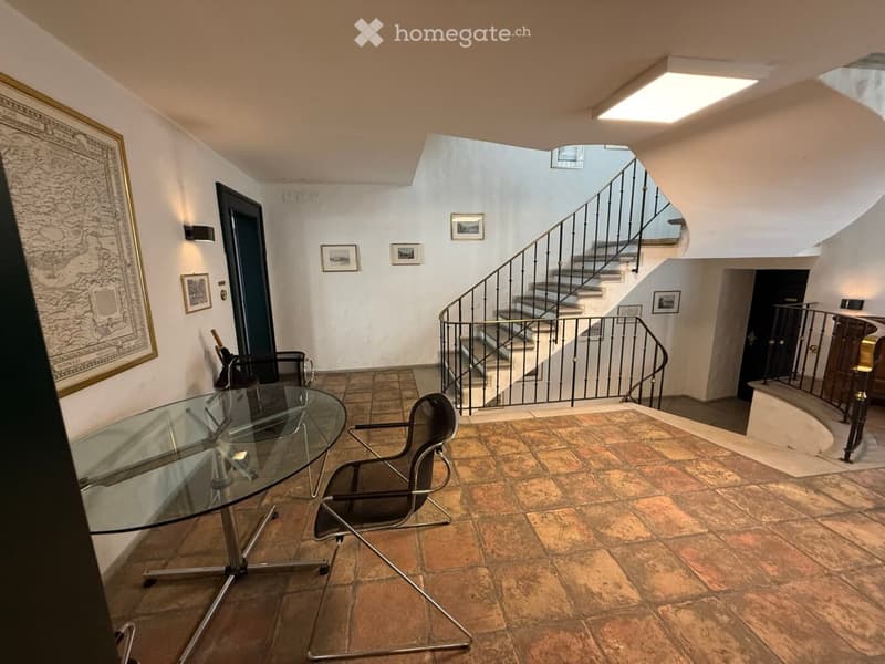 Hallway with a glass table and chairs, a staircase with a metal railing, and framed pictures on the walls.