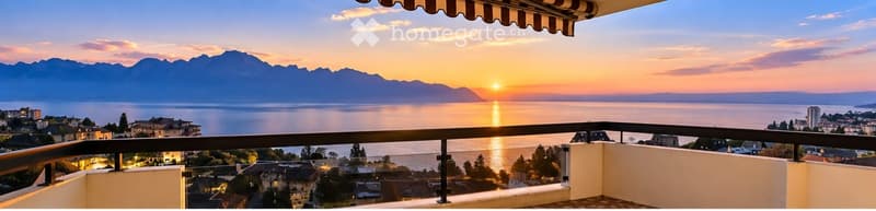 Balcony with a scenic view of a lake and mountains at sunset, featuring a railing and a striped awning.