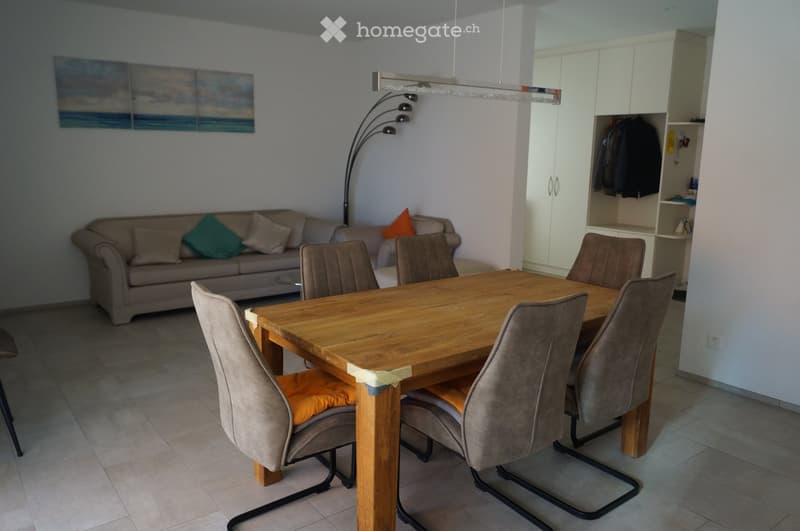 A modern living and dining area with a beige sofa, wooden dining table, six chairs, a floor lamp, and a white cabinet with coats hanging inside.