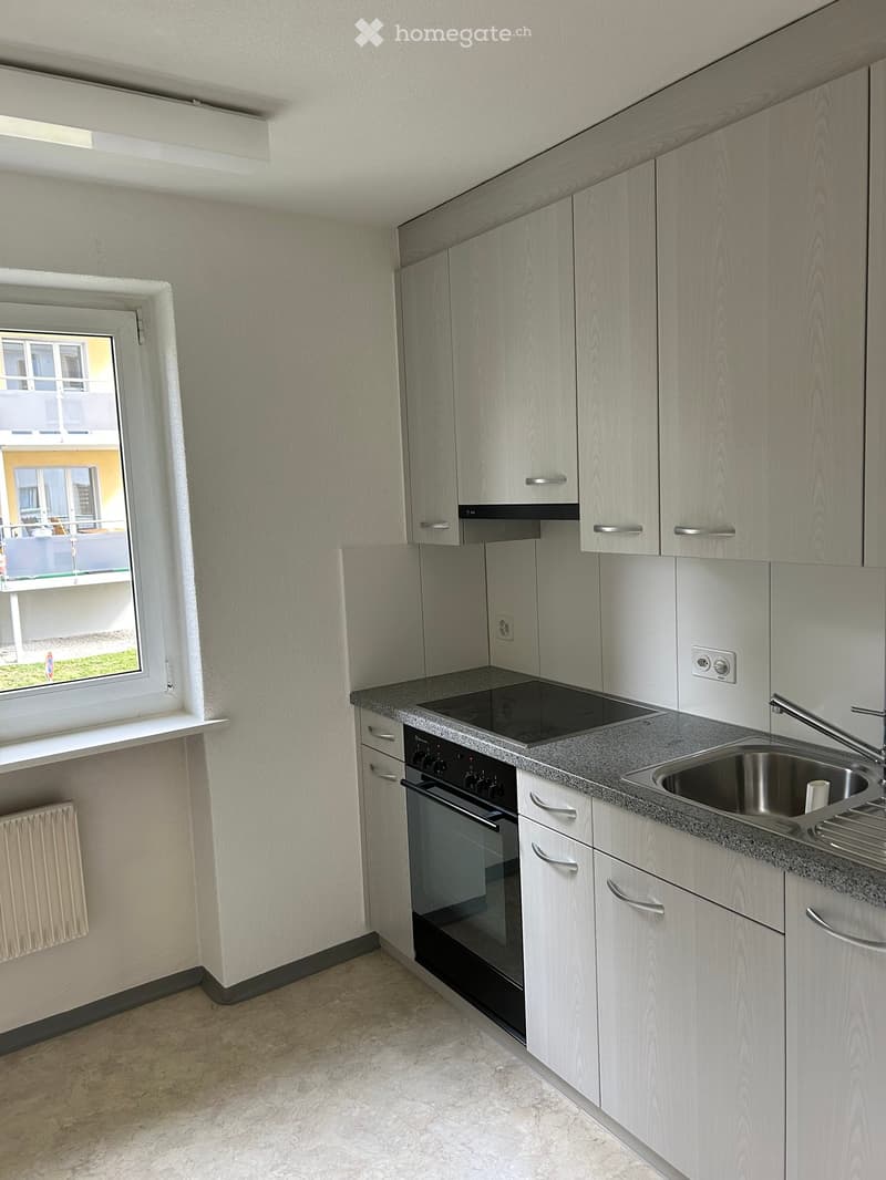 Modern kitchen with light wood cabinets, stainless steel sink, oven, and countertop. Features a window with a view of the outside.