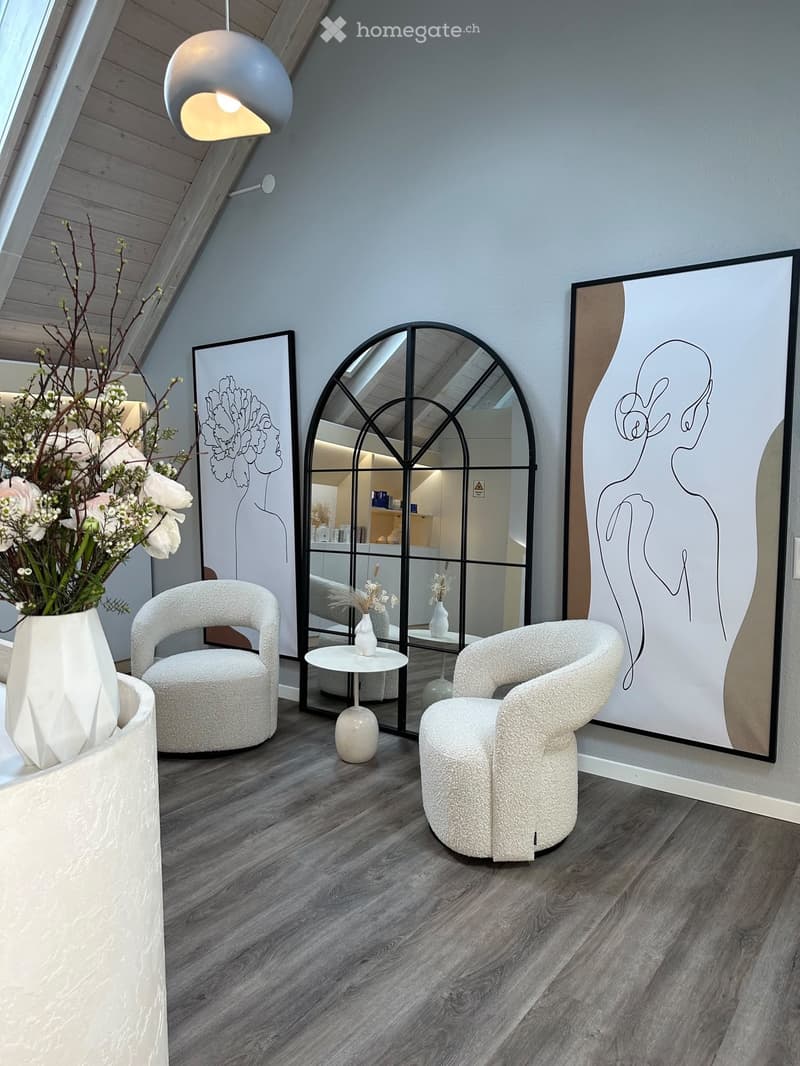 Modern living room with two round chairs, a small table, a vase with flowers, a large mirror, and artwork on the walls.