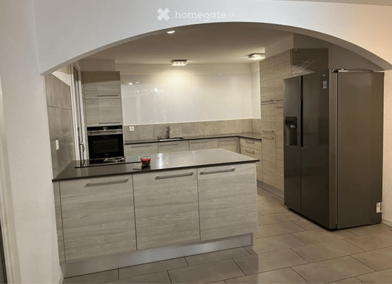 Modern kitchen with light wood cabinets, stainless steel appliances, and a central island with a black countertop.
