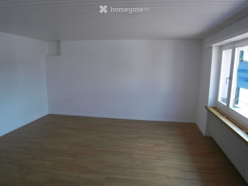 Empty room with wooden flooring and white walls, featuring a window with a wooden sill and a radiator below it.