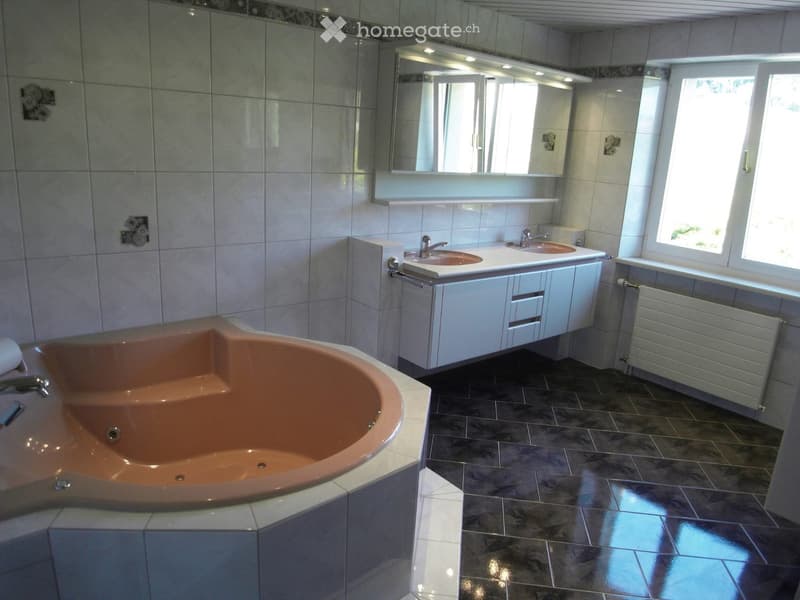 Modern bathroom with a large, curved bathtub, double sink vanity, and large mirror above the sink. The room features tiled walls and dark tiled flooring.