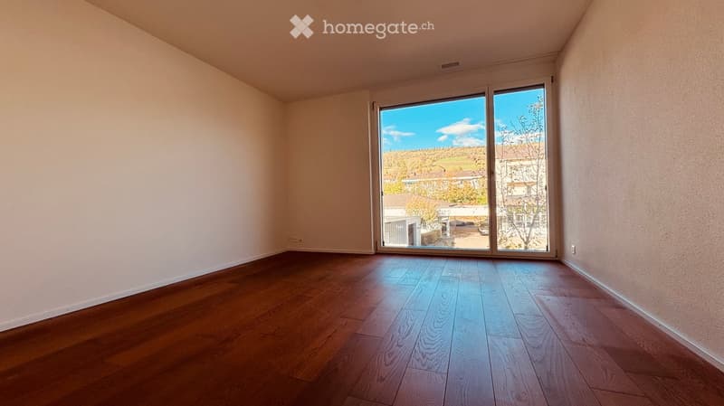 Empty room with wooden flooring and large sliding glass doors leading to a view of the outdoors.