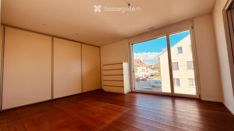 Empty room with wooden flooring, large sliding glass doors leading to a view of the street, and built-in storage units.