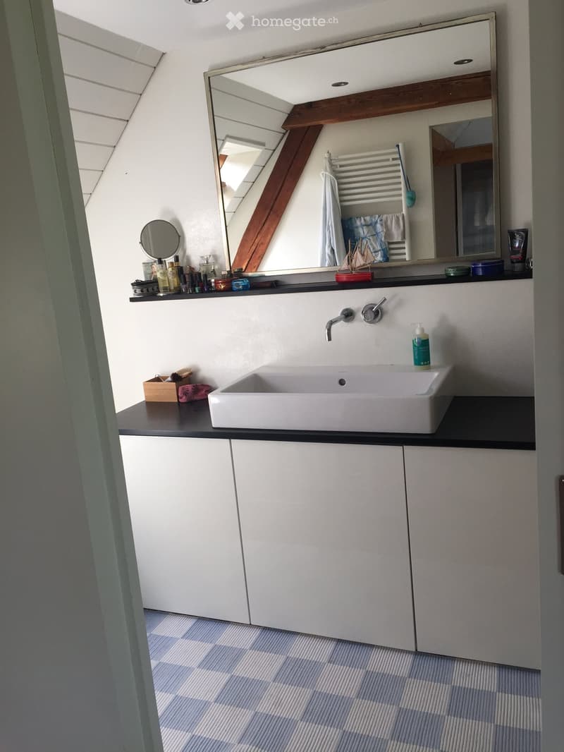 Modern bathroom with a white sink, large mirror, towel rack, and various toiletries on the counter.