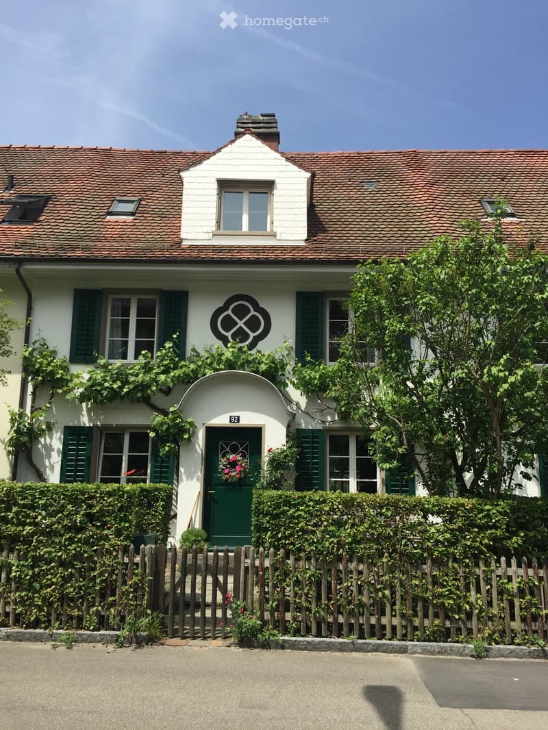 Two-story house with white walls, green shutters, red-tiled roof, and a decorative entrance featuring a wreath on the door.