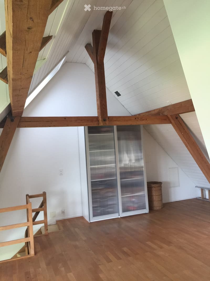 Empty attic space with wooden beams, white walls, wooden floor, glass cabinet, and a wicker basket.