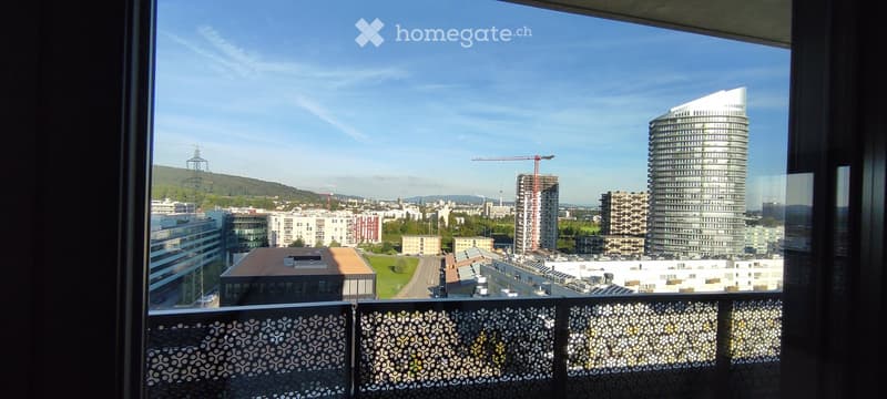 Balcony with a view of a cityscape, featuring modern high-rise buildings, a construction crane, and a clear blue sky.