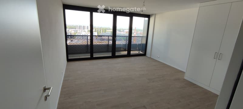 Empty room with wooden flooring, white walls, large sliding glass doors leading to a balcony with a city view.