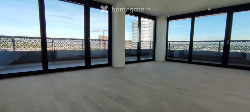 Empty room with large glass sliding doors leading to a balcony, wooden floor, white walls, and a view of a cityscape.
