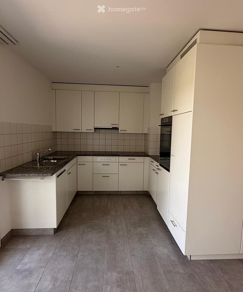 Modern kitchen with white cabinets, granite countertop, sink, and built-in oven. Grey tiled floor and walls.