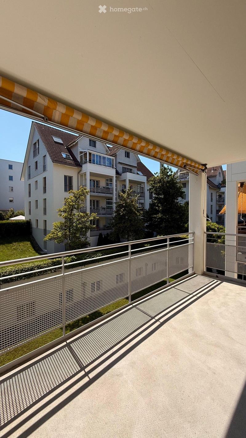 Balcony with metal railing, overlooking a residential area with houses, trees, and greenery.