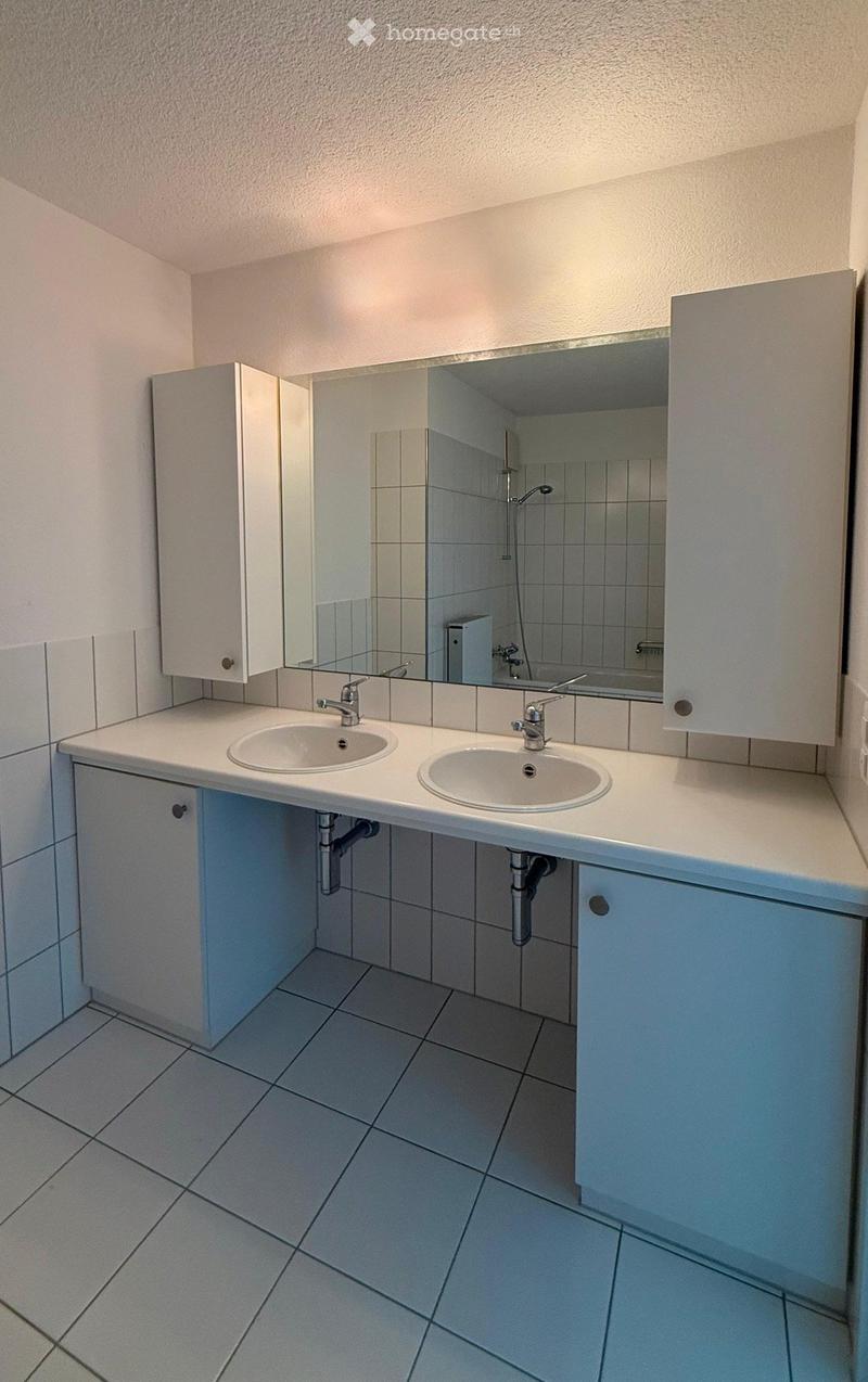 Modern bathroom with white tiled walls and floor, double sink vanity with mirrored cabinet, and built-in storage.