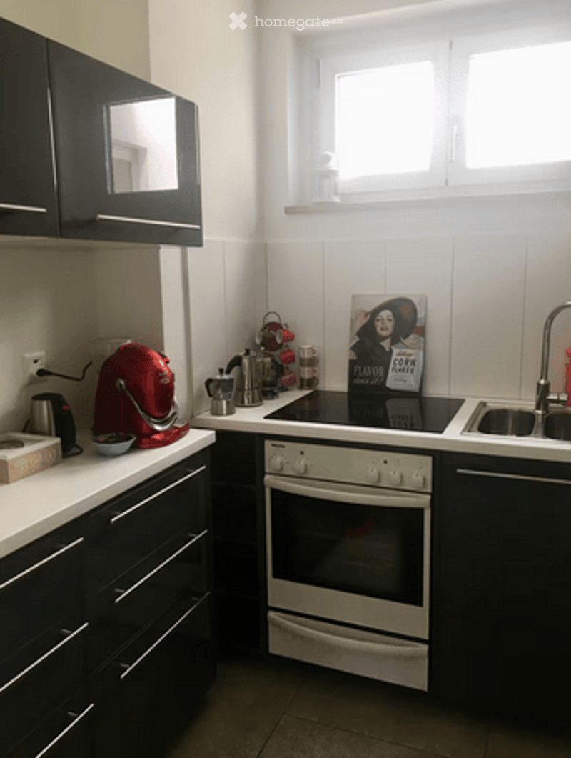 Modern kitchen with black cabinets, white countertops, and stainless steel appliances including a fridge, oven, and sink. A coffee maker and a framed picture are on the counter.