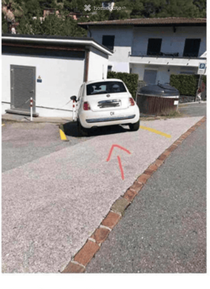 Parking area with marked spaces, a white car parked, and a building in the background.